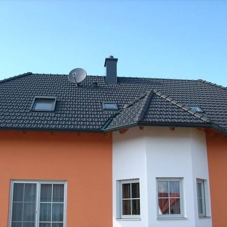 Oranges Haus mit weiß gestrichenem Anbau und dunklen Dachziegeln