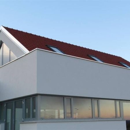 Ein Haus mit weißer Wand, rotem Dach und einer breiten Fensterfront