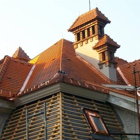 Ansicht eines Daches, dessen ober Hälfte mit roten Ziegeln eingedeckt ist, auf der unteren Hälfte sieht man ein Holzgerüst