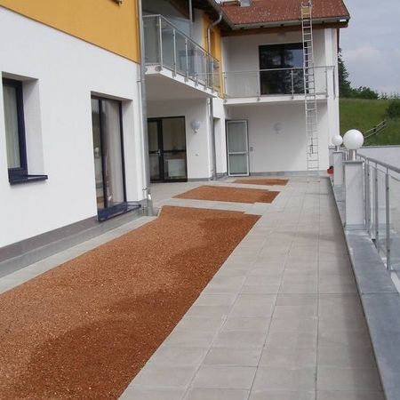 Mischung aus Flachdach und Terrasse, mit roten Steinen und grauen Bodenplatten ausgelegt und von einem Geländer umsäumt